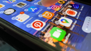 Close-up of a smartphone home screen with colorful app icons (Instagram, App Store, Pinterest) on a sunset background.