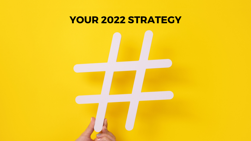 White hashtag held by hands against a bright yellow background, symbolizing a 2022 strategy plan.