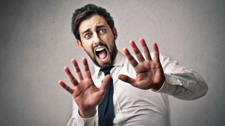 Man in a white shirt and dark tie raises hands in alarm, mouth open in a scream.
