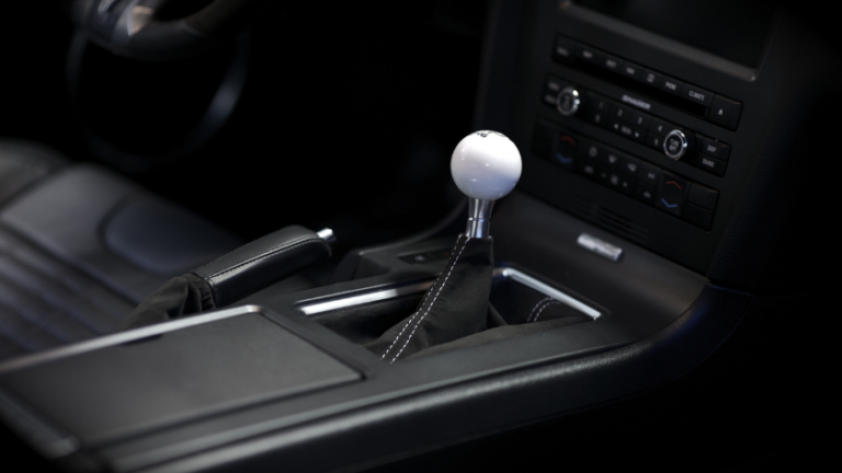 Manual gear shift lever with white knob in a car's center console area, surrounded by leather and controls