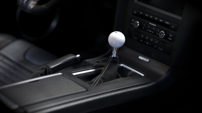 Manual gear shift lever with white knob in a car's center console area, surrounded by leather and controls