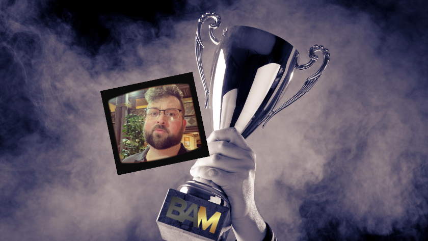 Hand holding a silver trophy with a small framed photo of a bearded man attached to the base.