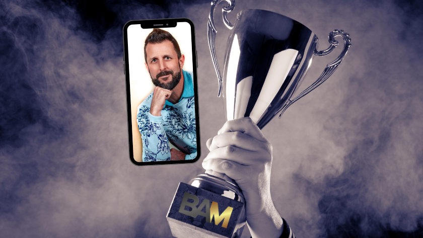 Silver trophy raised in smoke with a smartphone showing a bearded man beside it.