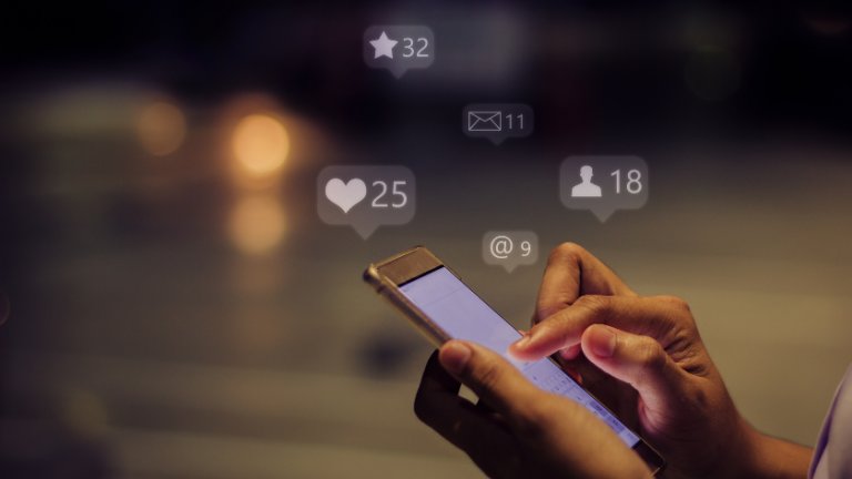 Hands holding a smartphone with floating social notifications above (likes, messages, followers, mentions).