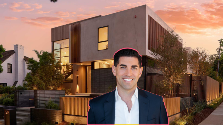Smiling real estate agent in a navy suit stands in front of a modern two‑story house at sunset.