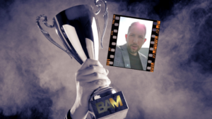A hand raises a silver trophy labeled 'BAM' with a film strip showing a man's selfie beside it.