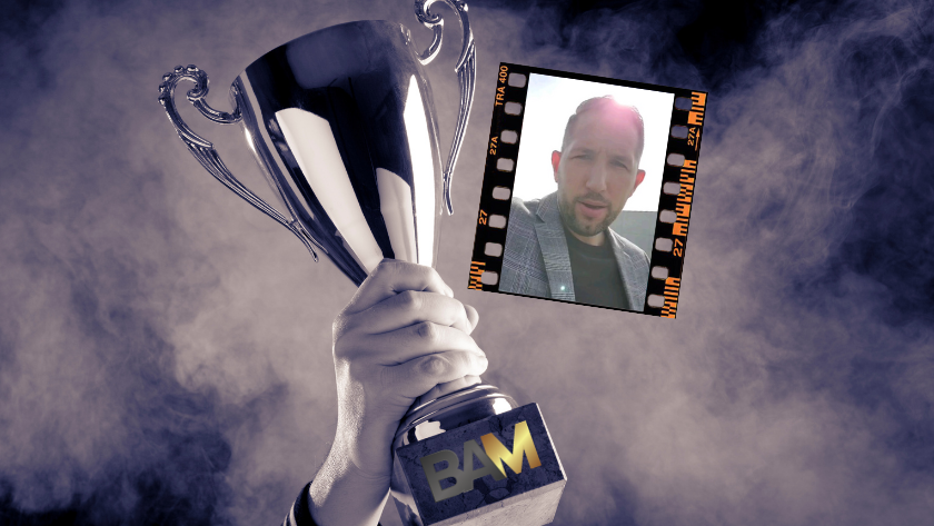 A hand raises a silver trophy labeled 'BAM' with a film strip showing a man's selfie beside it.