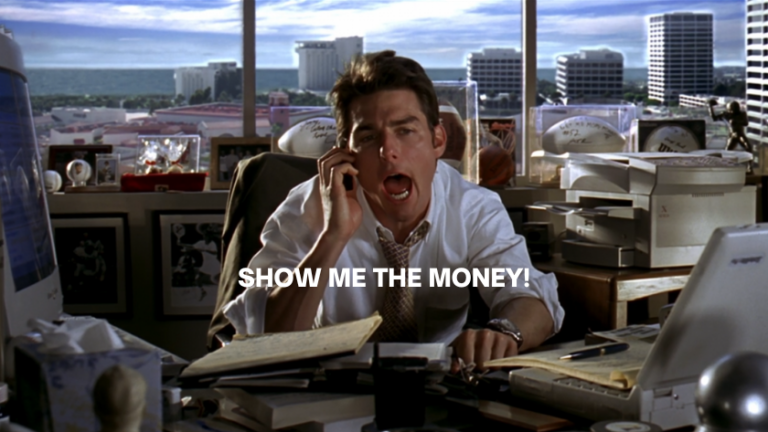 Businessman on a phone at a cluttered desk, shouting the line “Show me the money” with a city view outside the windows.