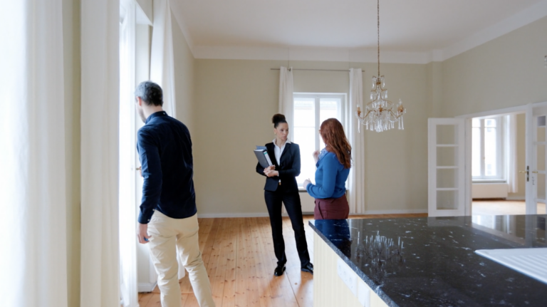 Three professionally dressed adults stand in a bright room with white curtains, chatting near a marble kitchen island.
