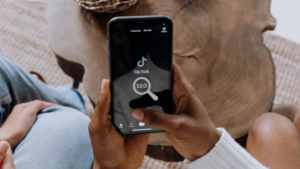 Person holding a smartphone displaying the TikTok app with a magnifying-glass icon labeled SEO in the foreground.