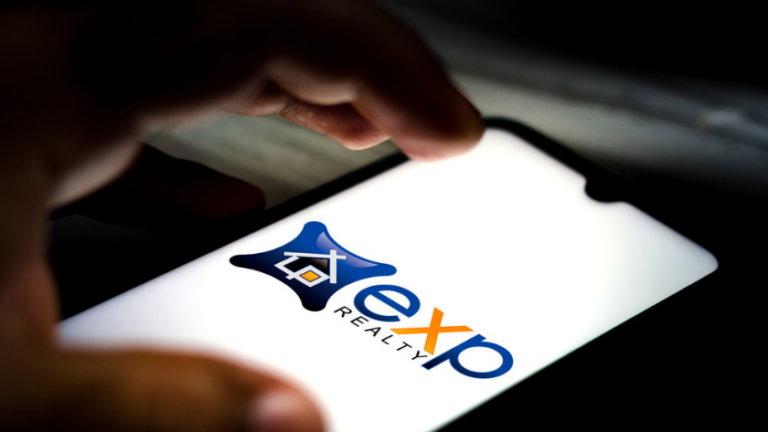 Close-up of a hand holding a smartphone showing a real estate logo with the word REALTY on the screen.