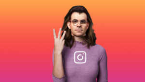 Person in a purple sweater with the Instagram logo on the chest, gesturing with three fingers against an orange‑pink gradient background.