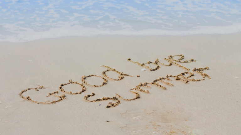 'Good vibes' written in wet sand on a sunny beach with gentle waves in the background