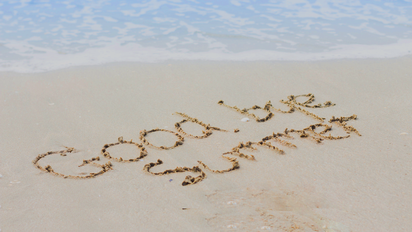 'Good vibes' written in wet sand on a sunny beach with gentle waves in the background