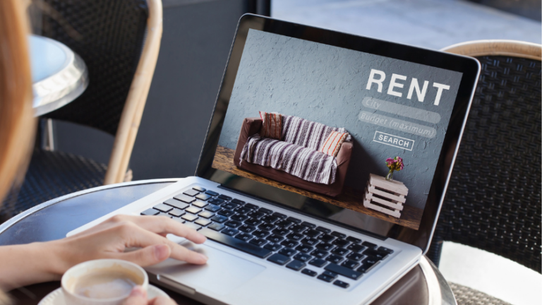 Laptop on a cafe table displaying a furniture rental website with a striped sofa image and a search bar labeled RENT