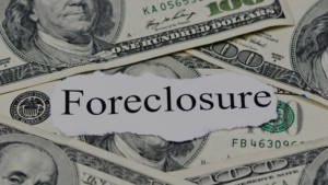 Torn paper reading Foreclosure laid over scattered U.S. dollar bills, signaling financial distress