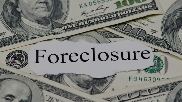 Torn paper reading Foreclosure laid over scattered U.S. dollar bills, signaling financial distress