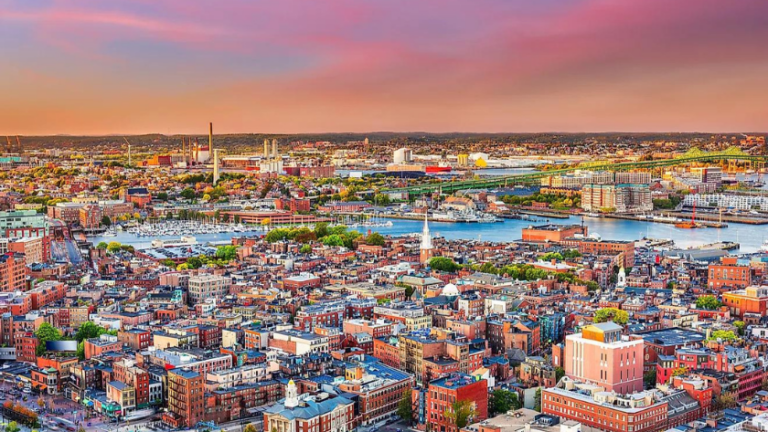 Aerial view of a coastal city with colorful brick buildings and a waterfront at sunset.