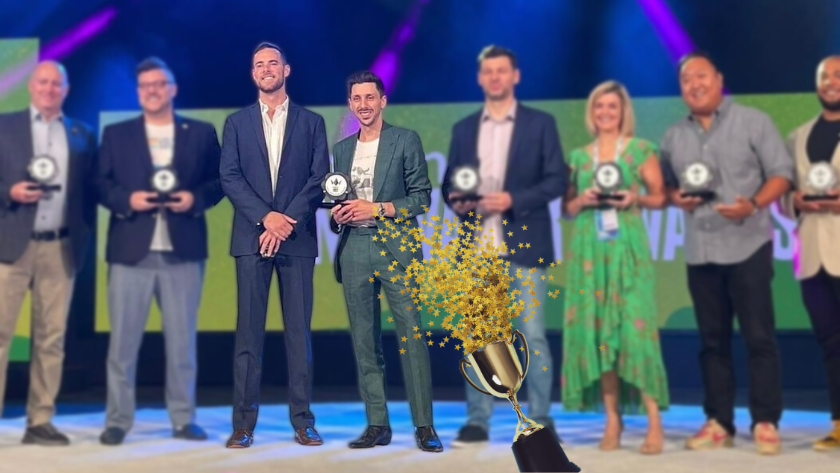 Eight award recipients on-stage posing with trophies, a large gold trophy graphic in the foreground.