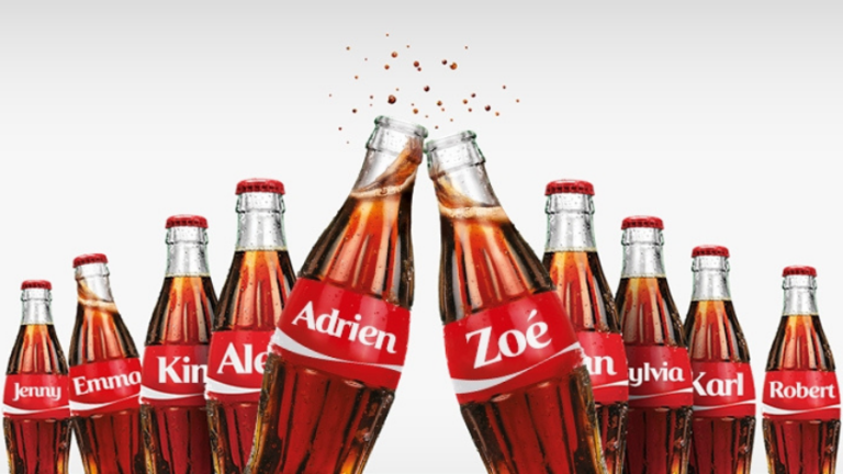 Row of glass Coca-Cola bottles with red name labels, tilted together in the center (Adrien and Zoe prominent)