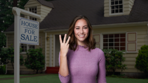 Smiling woman in a pink sweater stands in front of a beige house with a 'House for Sale' sign in the yard