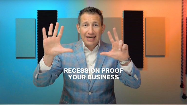 Man in a light blue blazer speaks to camera with hands raised, the text 'Recession Proof Your Business' overlaid in white. Background shows sound panels and colorful lighting.