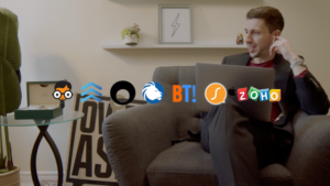 Businessman in a suit on a gray couch with a laptop, talking on the phone; sponsor logos overlay the scene.
