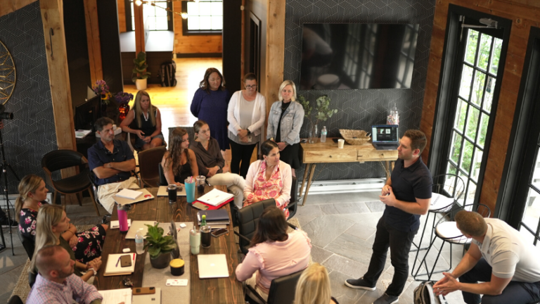 Group of people in a rustic conference room listening to a presenter standing near a laptop.