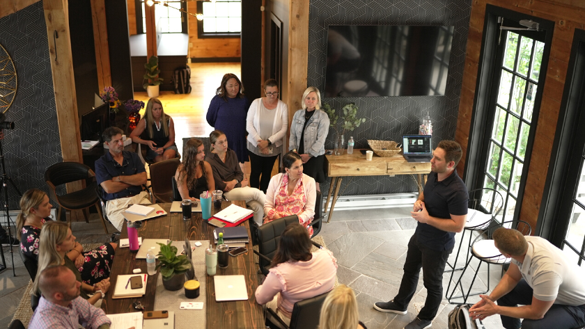 Group of people in a rustic conference room listening to a presenter standing near a laptop.