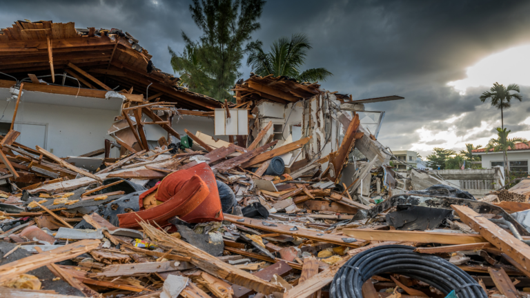 Collapsed house and debris scattered across a street after a hurricane, with a dark, stormy sky overhead