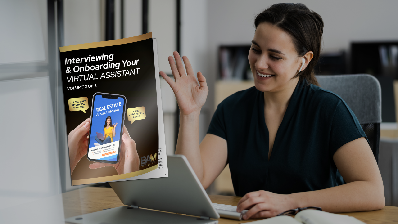 Smiling woman at a desk wearing wireless earbuds waves hello; a poster about interviewing virtual assistants is beside her.