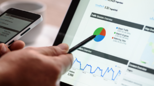 Person using a stylus to view an analytics dashboard with a pie chart and line graph on a tablet/monitor