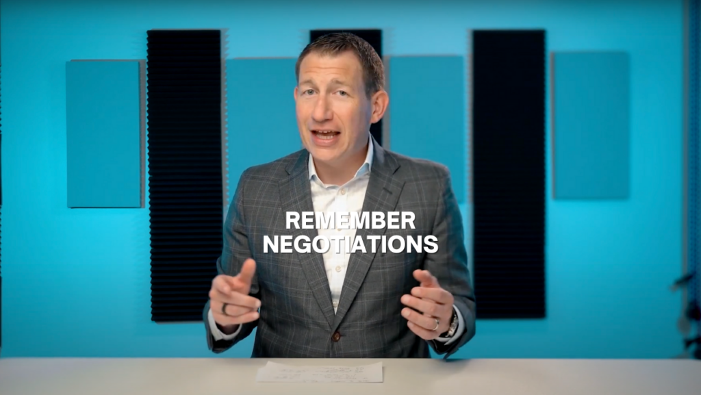 Presenter in a gray suit sits at a desk in a blue‑toned studio with 'REMEMBER NEGOTIATIONS' overlay text, delivering a tip video.