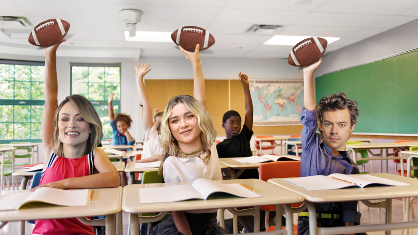 Diverse students in a bright classroom raise their hands, each holding a football, seated at desks with notebooks open.