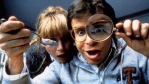 Two friends lean in, peering through oversized magnifying glasses at the camera with amused expressions.
