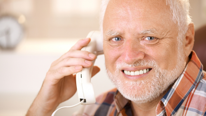 Smiling senior man on a white landline phone, wearing a plaid shirt, indoors in a cozy setting.