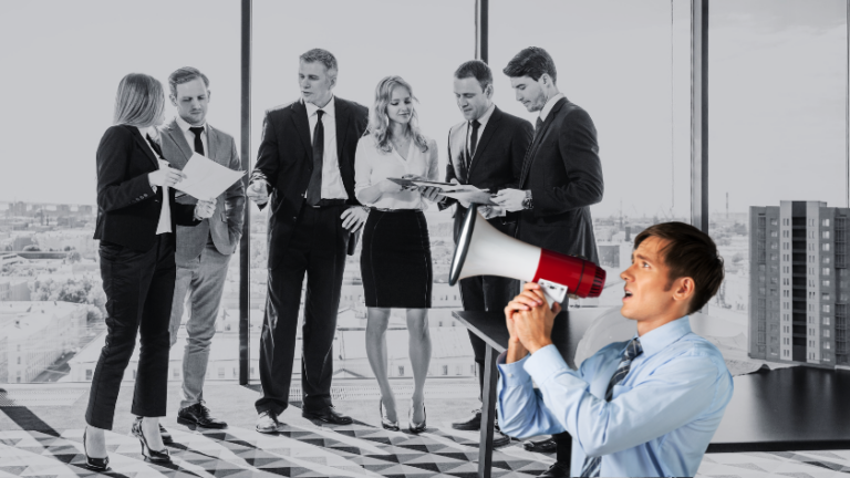 Six business professionals in suits discuss documents in a glass-walled office as a man in the foreground speaks into a megaphone to address them.