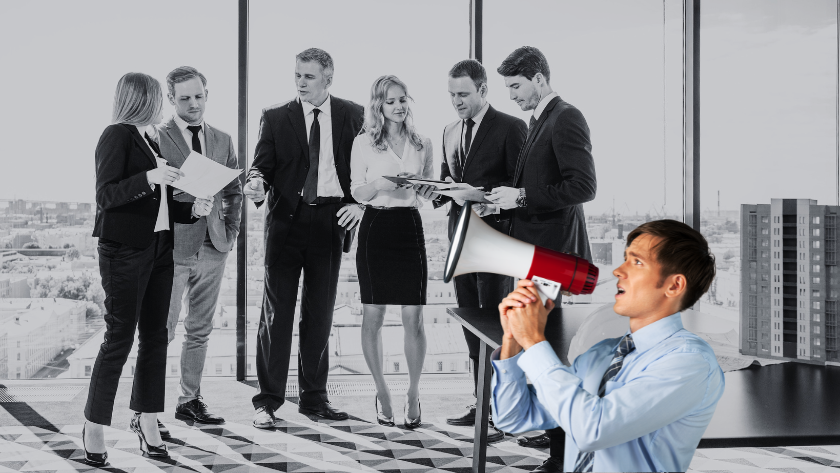 Six business professionals in suits discuss documents in a glass-walled office as a man in the foreground speaks into a megaphone to address them.