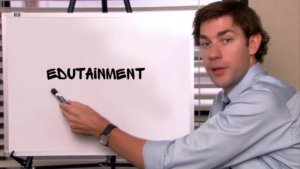 Man in a shirt points to a whiteboard with the word 'EDUTAINMENT' written on it during a presentation.