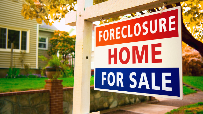Sign reading 'FORECLOSURE HOME FOR SALE' hanging on a white post in a suburban yard.