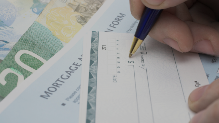 Close-up of a hand writing on a mortgage check form with a blue pen and cash in the background.