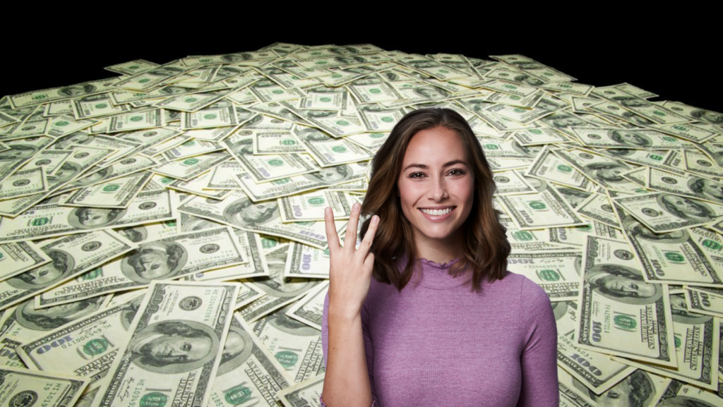Smiling woman in a pink sweater stands in front of a huge pile of US hundred-dollar bills, suggesting wealth or reward.