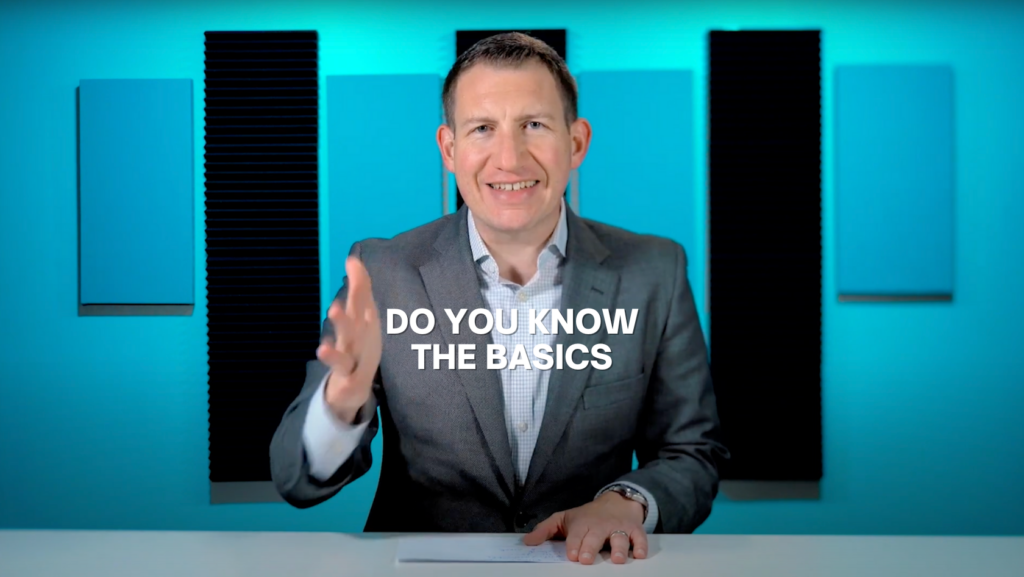 Smiling man in a gray suit speaks at a desk in a blue studio; bold caption reads 'DO YOU KNOW THE BASICS'.