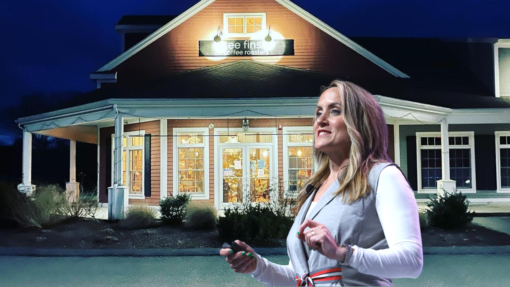 Smiling woman in a light gray blazer with white sleeves stands outside a warmly lit coffee shop at night.