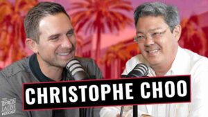 Two men sit at microphones in a podcast studio, smiling during an interview with a bold “CHRISTOPHE CHOO” banner across the foreground.