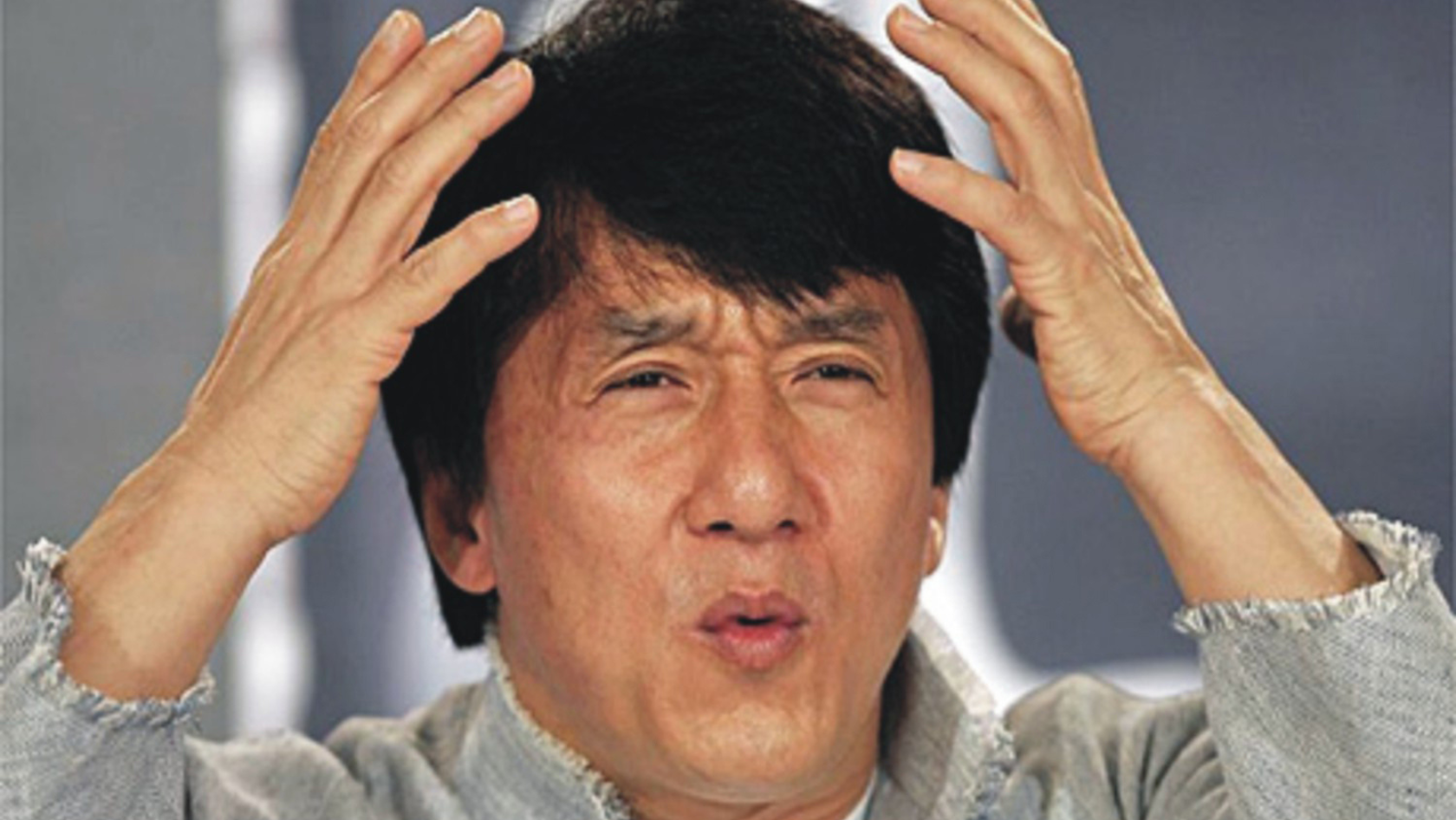 Man with short black hair holds his head with both hands, a distressed or frustrated expression on his face.