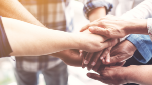 Hands from multiple people join together in a show of teamwork and support.