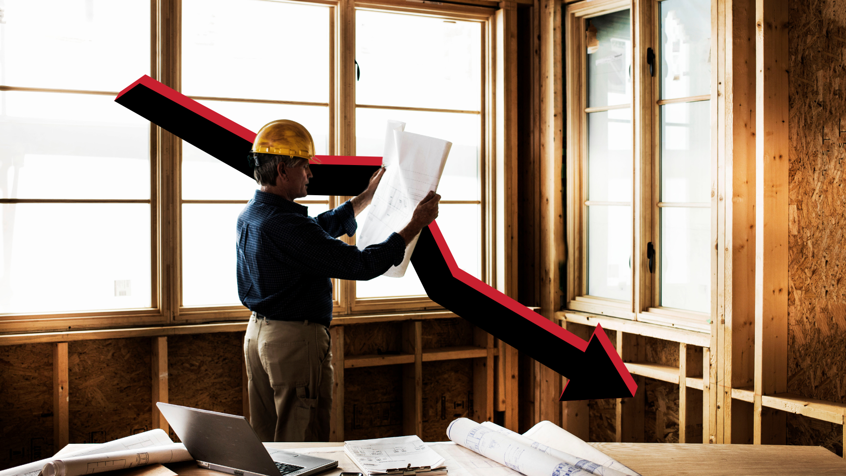 Construction worker with a yellow hard hat reviewing blueprints inside an unfinished wooden room, overlaid by a red and black downward arrow.