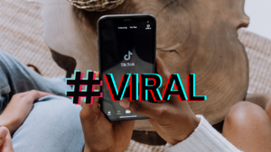 Close-up of hands holding a smartphone showing the TikTok app with a bold, colorful '#VIRAL' overlay text.