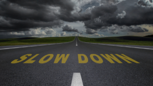 Long road toward the horizon with yellow 'SLOW DOWN' painted on the pavement under a stormy sky.